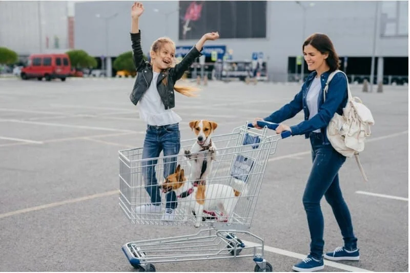 Happy young mother, daughter and their two dogs in shopping cart preparing their new puppy checklist