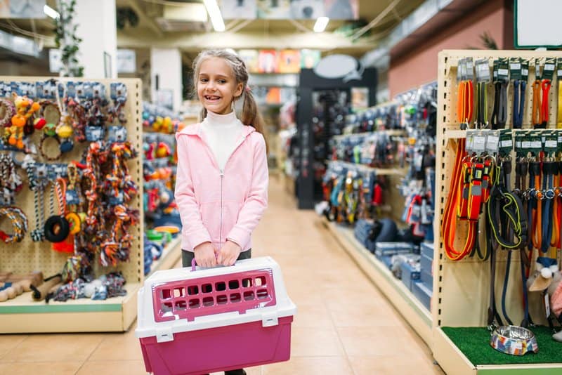 Happy little girl with carrier for cat in pet shop