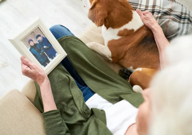 An elderly lady sitting beside a dog while holding a picture frame on the couch